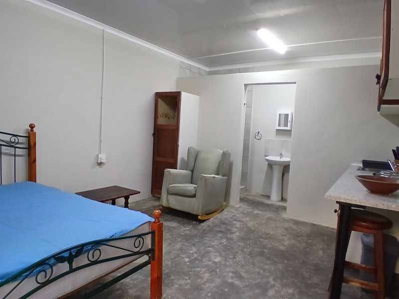 Open-plan studio cottage featuring a kitchenette area and an en-suite bathroom with a pedestal basin, finished with basic concrete flooring.