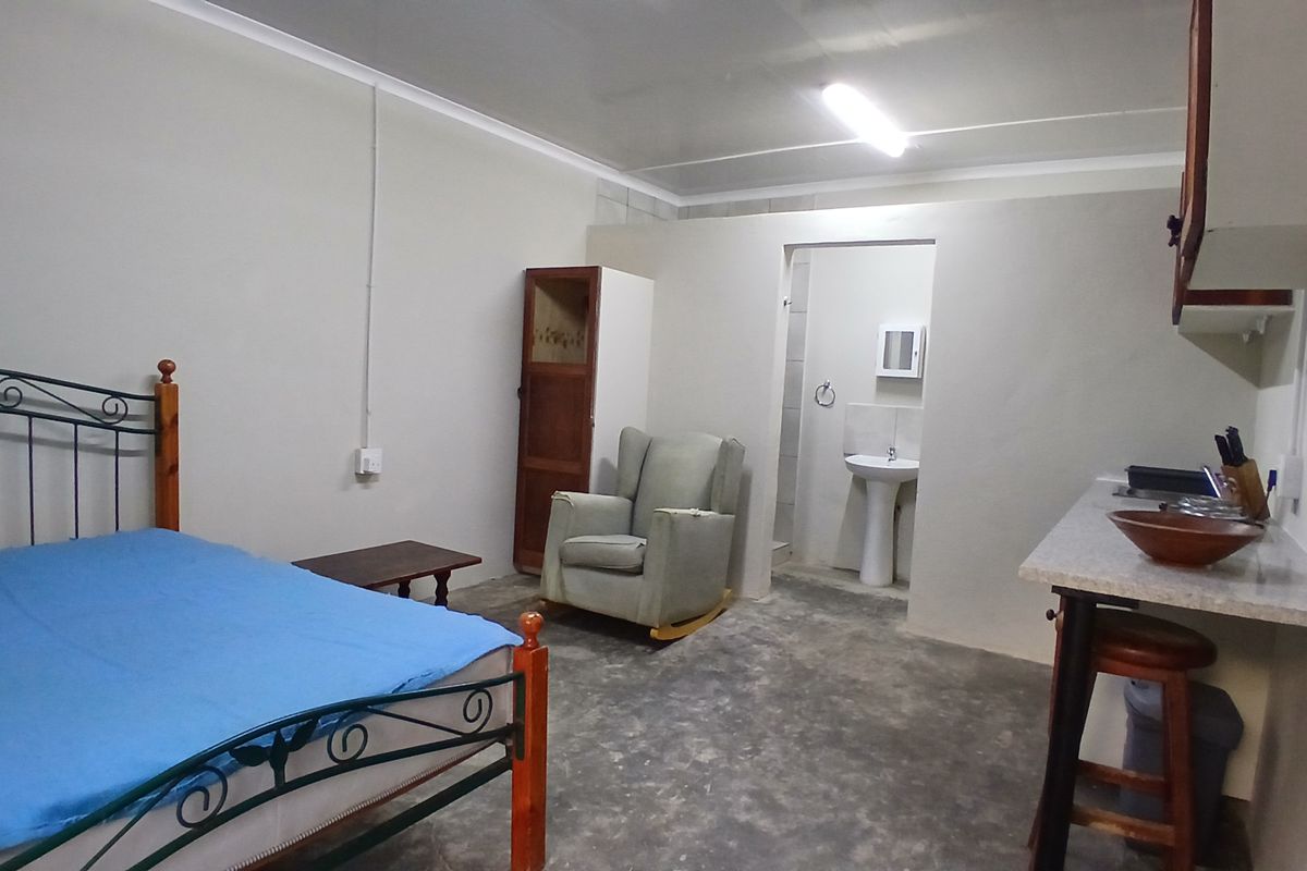 Open-plan studio cottage featuring a kitchenette area and an en-suite bathroom with a pedestal basin, finished with basic concrete flooring.