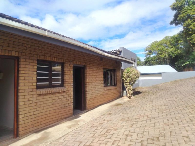 Exterior view of a face brick cottage featuring a paved driveway, tiled roof, and aluminium window frames.