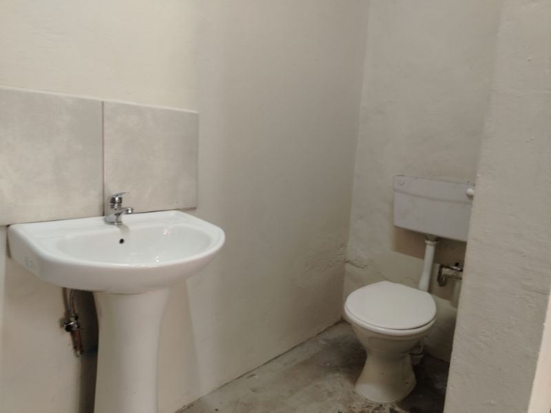 A basic bathroom featuring a pedestal basin and toilet with a tiled splashback, currently in need of cosmetic updates and floor finishing.