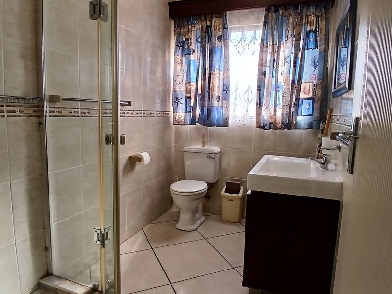 A functional bathroom featuring a glass shower enclosure, vanity basin, and neutral ceramic tiling throughout.