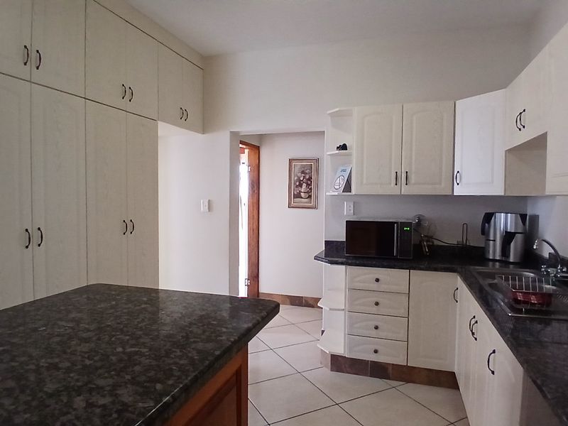 A functional kitchen featuring ample built-in cabinetry, granite countertops, tiled flooring, and a double sink, offering a practical layout for daily use.