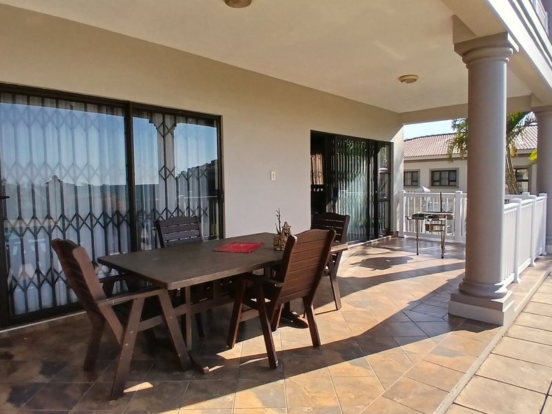 A spacious covered patio featuring tiled flooring, structural columns, and sliding glass doors with security gates, providing a seamless transition to the outdoor area.
