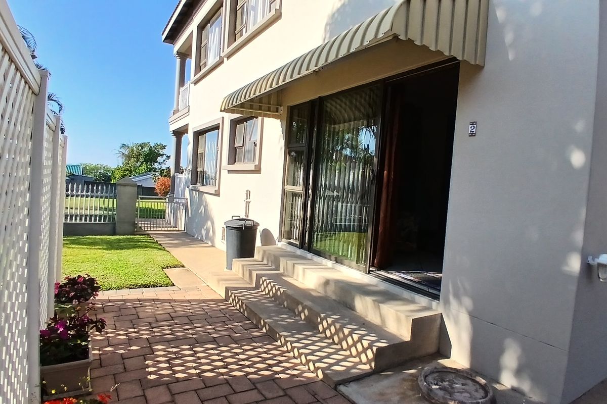 Rear exterior view of the apartment featuring a paved patio area, sliding glass door access, and a canvas awning over the entrance.