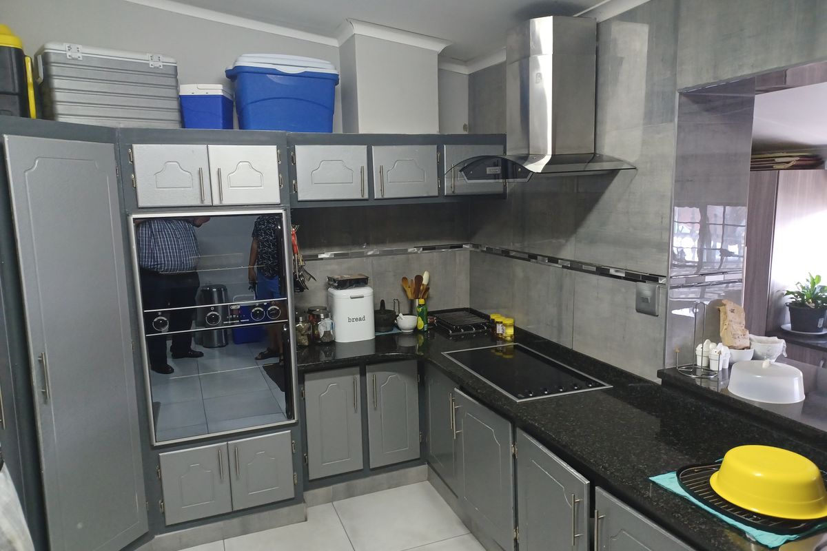 A functional kitchen featuring dark granite countertops, grey cabinetry, a built-in oven, and a stainless steel extractor fan.