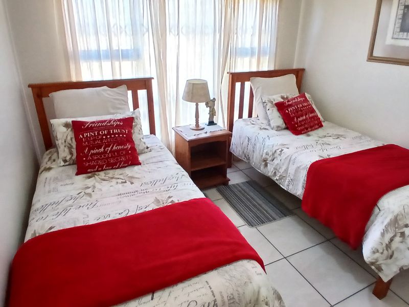 A functional bedroom featuring tiled flooring and large windows with curtain rails, providing natural light to the space.