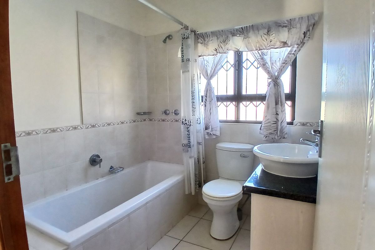 A functional bathroom featuring a built-in bathtub with shower, a toilet, and a vanity basin with a granite countertop.