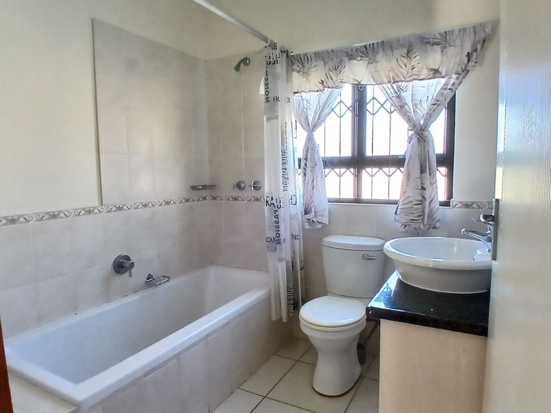 A functional bathroom featuring a built-in bathtub with shower, a toilet, and a vanity basin with a granite countertop.