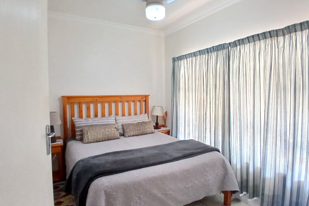 A functional bedroom featuring a ceiling fan and large window with curtain tracks, providing a neutral space ready for personalization.