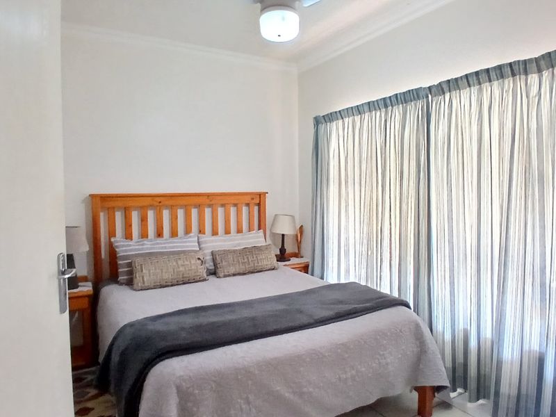 A functional bedroom featuring a ceiling fan and large window with curtain tracks, providing a neutral space ready for personalization.