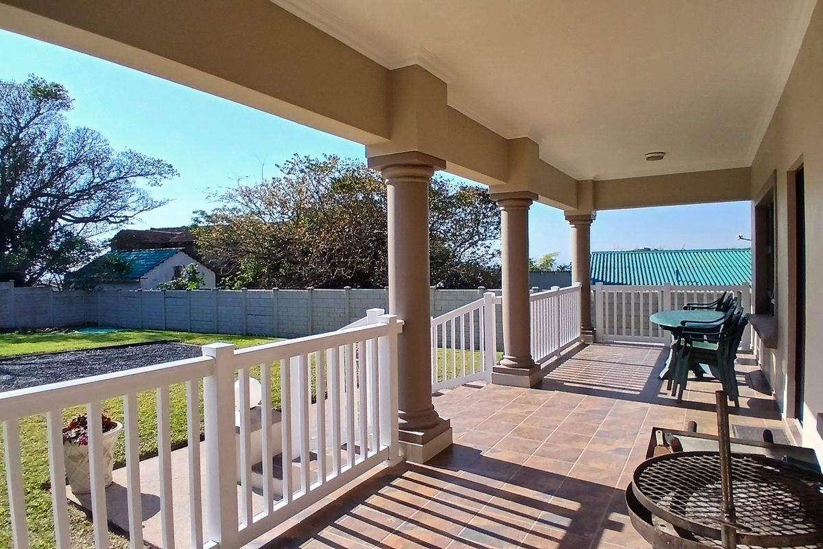 A spacious covered patio featuring tiled flooring, classic columns, and a white balustrade railing, overlooking a private garden area.