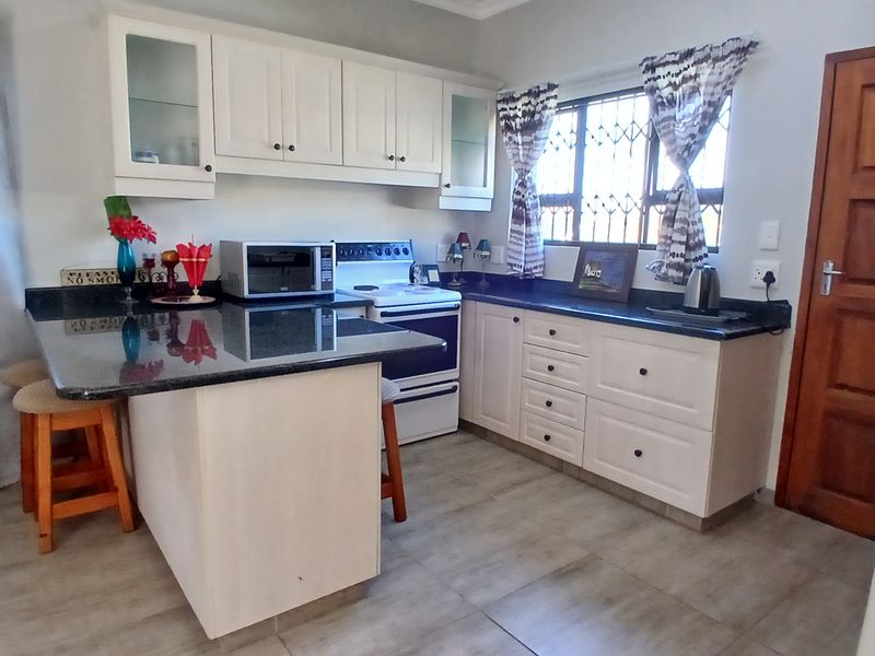 A functional kitchen featuring white cabinetry, dark granite countertops, a freestanding stove, and tiled flooring with a window security gate.