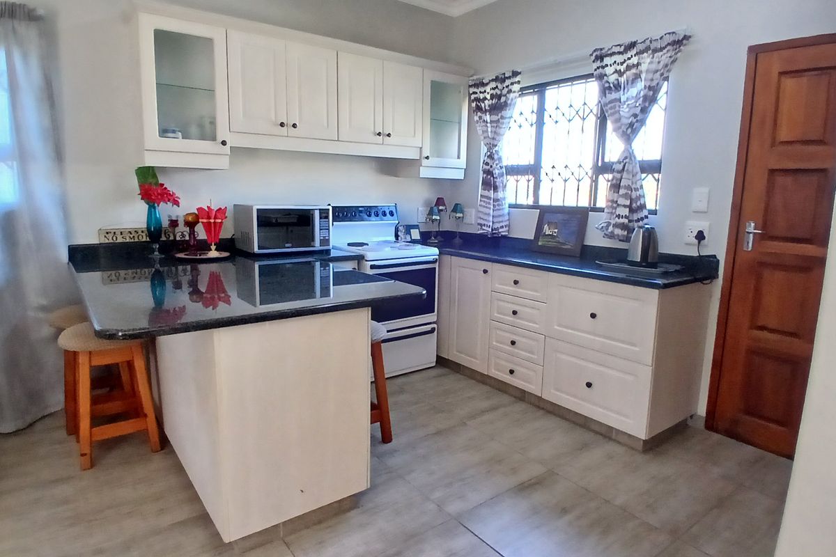 A functional kitchen featuring white cabinetry, dark granite countertops, a freestanding stove, and tiled flooring with a window security gate.