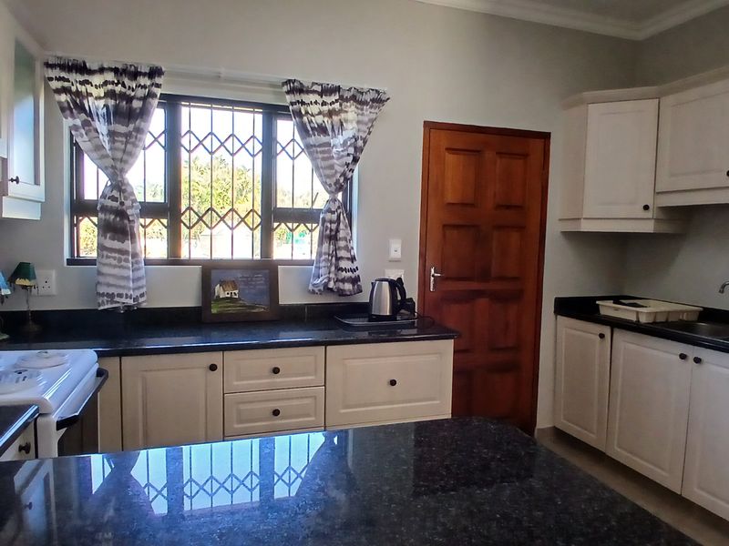 A functional kitchen featuring granite countertops, ample built-in cabinetry, and a double sink, with natural light entering through a window with security bars.
