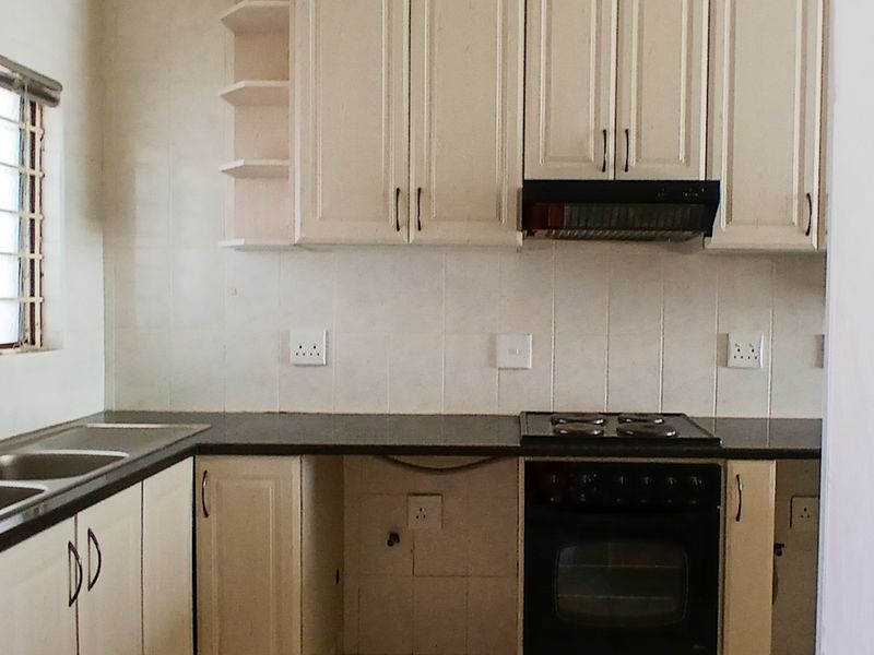 A functional kitchen featuring built-in cabinetry, granite countertops, a double sink, and integrated cooking appliances including an oven, hob, and extractor fan.