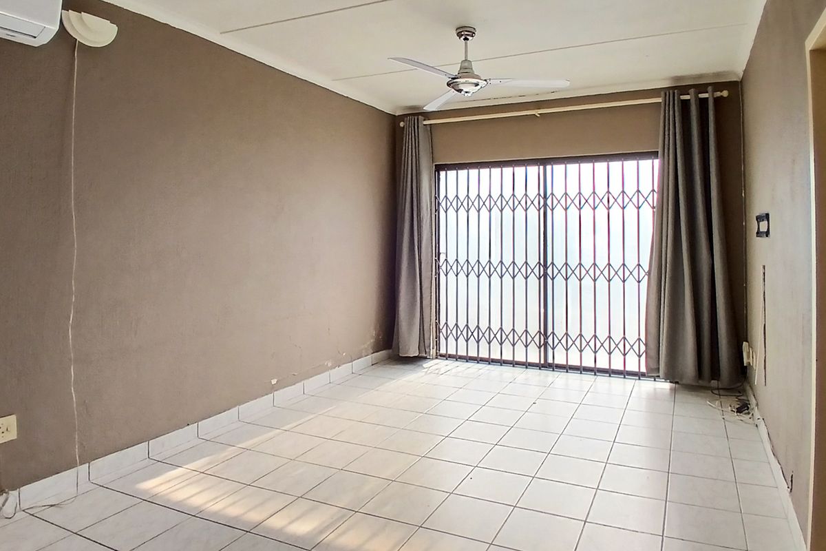 An empty living room featuring tiled flooring, a ceiling fan, air conditioning, and a sliding door with a security gate.