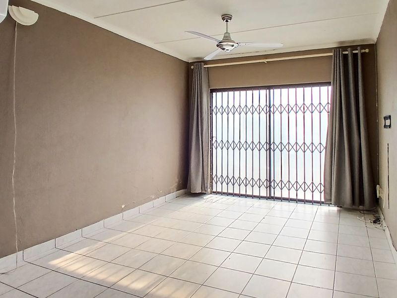 An empty living room featuring tiled flooring, a ceiling fan, air conditioning, and a sliding door with a security gate.