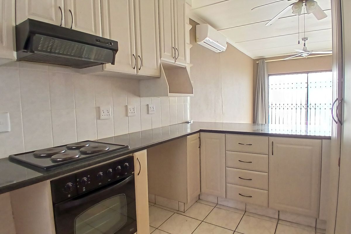 A functional kitchen featuring built-in cabinetry, an electric stove with oven, tiled backsplash, and tiled flooring, with an adjacent air-conditioned living area.