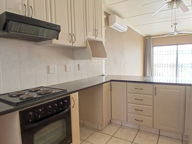 A functional kitchen featuring built-in cabinetry, an electric stove with oven, tiled backsplash, and tiled flooring, with an adjacent air-conditioned living area.