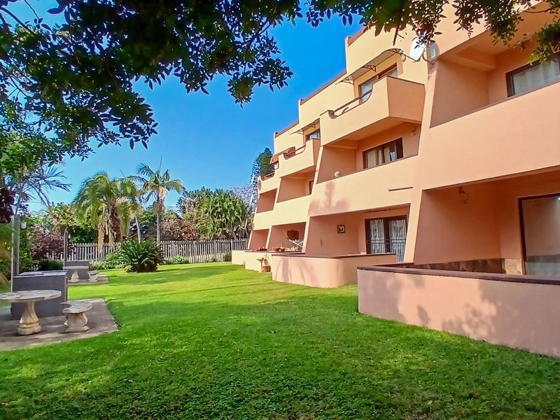 Rear view of the apartment complex featuring private balconies, sliding glass doors, and a well-maintained communal garden with stone seating areas.