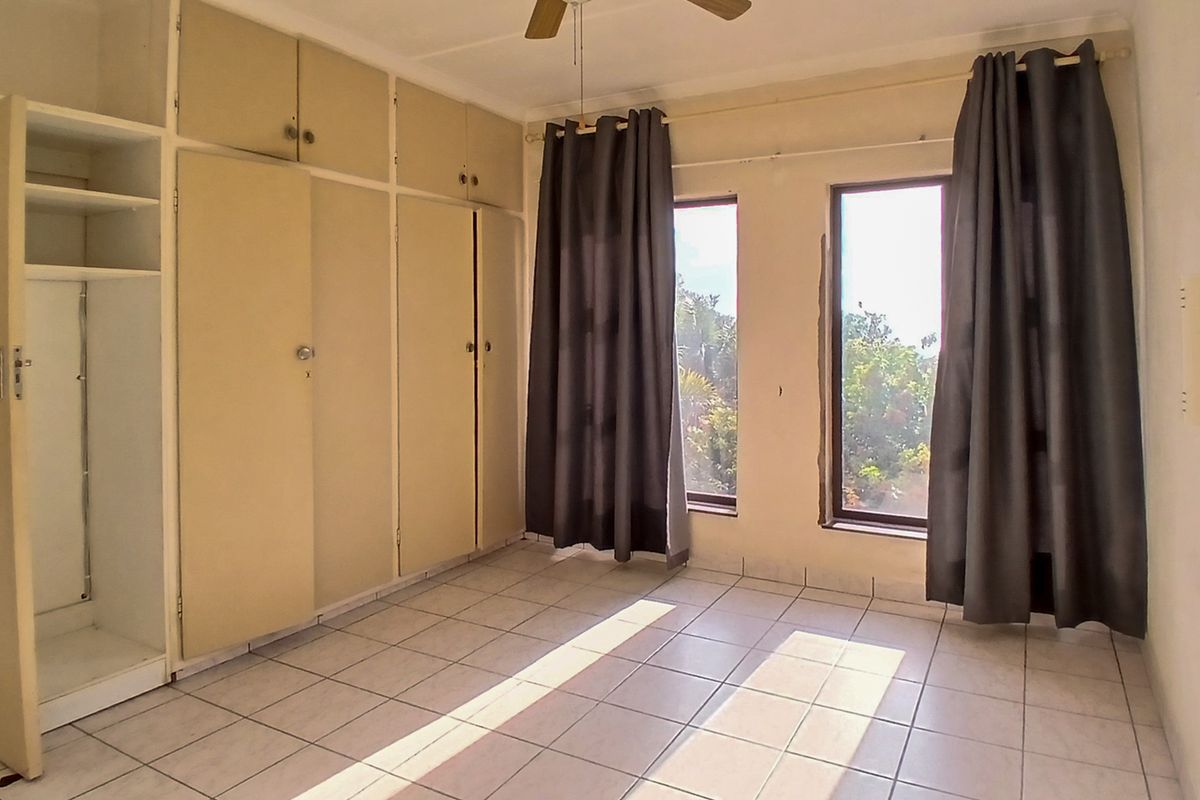 A vacant bedroom featuring tiled flooring, built-in cupboards with overhead storage, and a ceiling fan, offering a blank canvas for renovation.