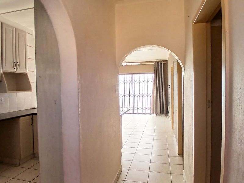 An open-plan apartment interior featuring a kitchen with granite countertops, tiled flooring, and arched architectural details leading to a living area with security gate.