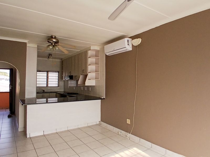 Open-plan living area featuring a functional kitchen with granite countertops, tiled flooring, and a wall-mounted air conditioning unit.