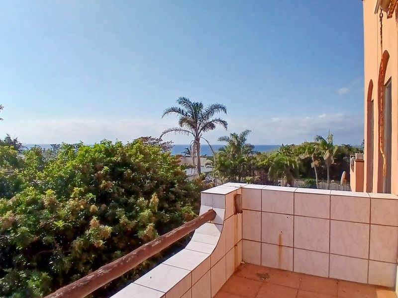 A balcony featuring tiled surfaces and a railing, offering an elevated outdoor space with views of the surrounding greenery and distant ocean.