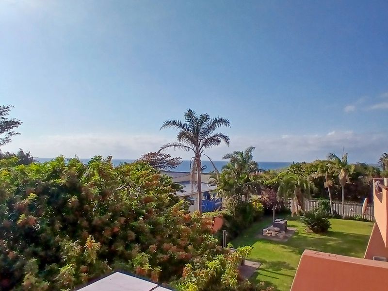 Elevated view overlooking a landscaped garden and coastal horizon from an apartment balcony.