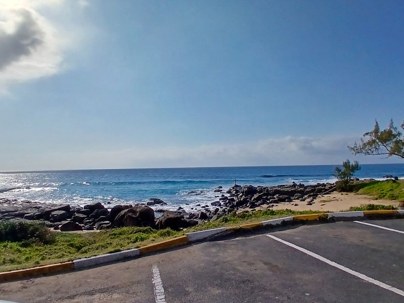 A scenic coastal view overlooking the ocean and rocky shoreline, featuring an adjacent paved parking area with marked bays.