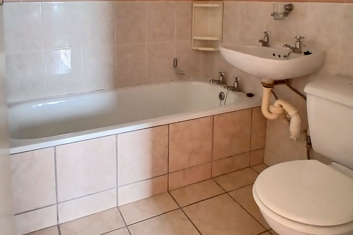 A functional bathroom featuring a bathtub, pedestal basin, and toilet with neutral wall and floor tiling.