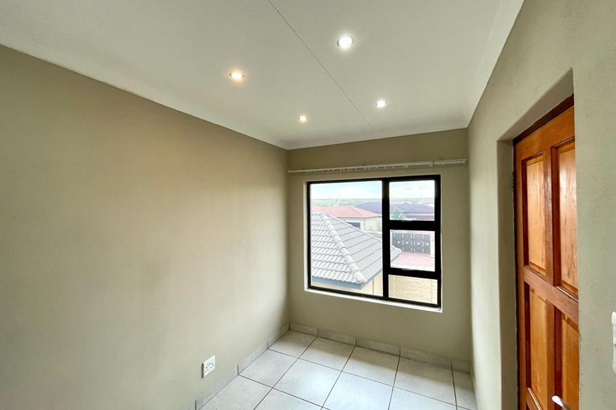A bright, empty bedroom featuring neutral wall tones, tiled flooring, recessed ceiling lighting, and a window with views of the surrounding neighborhood.