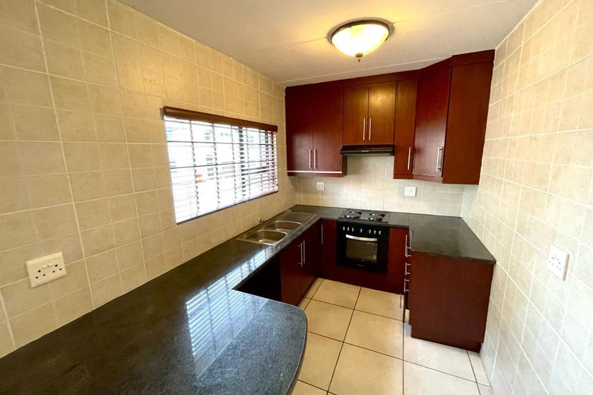 A functional kitchen featuring dark wood cabinetry, granite countertops, a built-in oven and hob, and fully tiled walls.