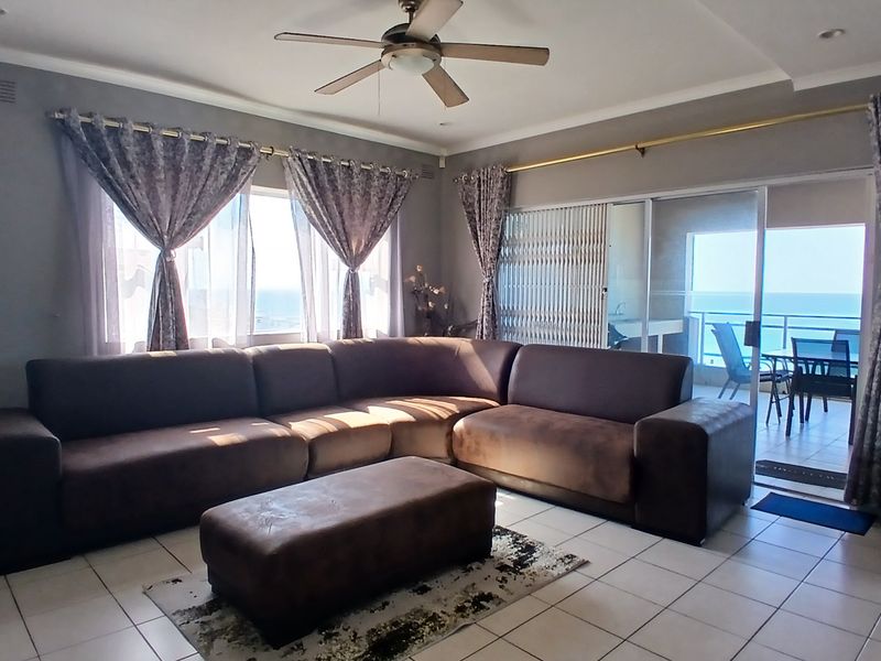 Spacious living room featuring tiled flooring, a ceiling fan, and large sliding glass doors that open onto a balcony with ocean views.