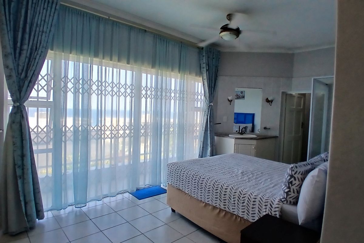 Spacious bedroom featuring tiled flooring, a ceiling fan, and a built-in vanity area with direct access to a balcony through a sliding security door.