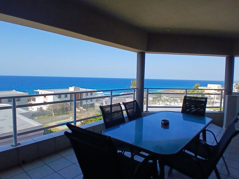 Spacious covered balcony featuring tiled flooring and a metal balustrade, offering expansive ocean and coastal views.