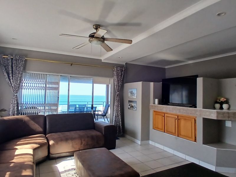 Spacious living room featuring tiled flooring, a ceiling fan, and large sliding glass doors that open to a balcony with ocean views.