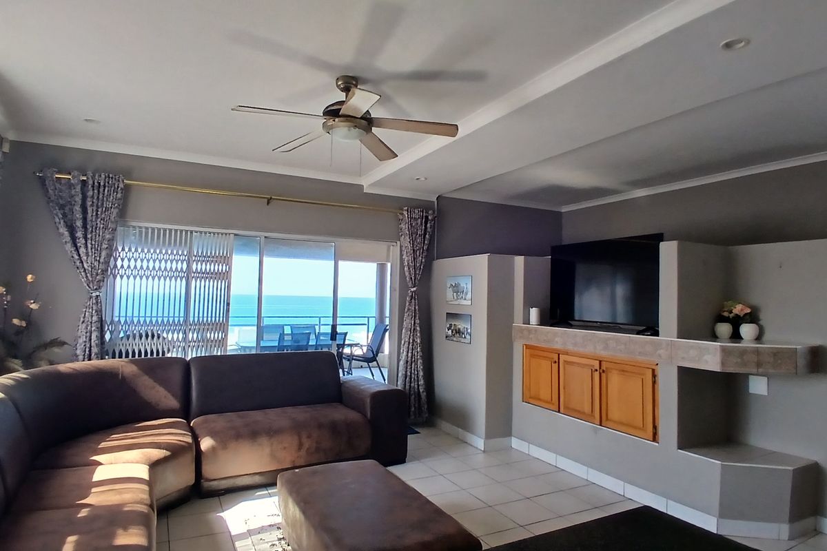 Spacious living room featuring tiled flooring, a ceiling fan, and large sliding glass doors that open to a balcony with ocean views.