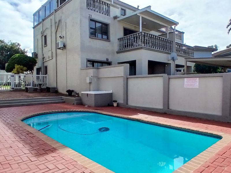 Outdoor pool area featuring a swimming pool with brick paving, a boundary wall, and a multi-story building with balconies.