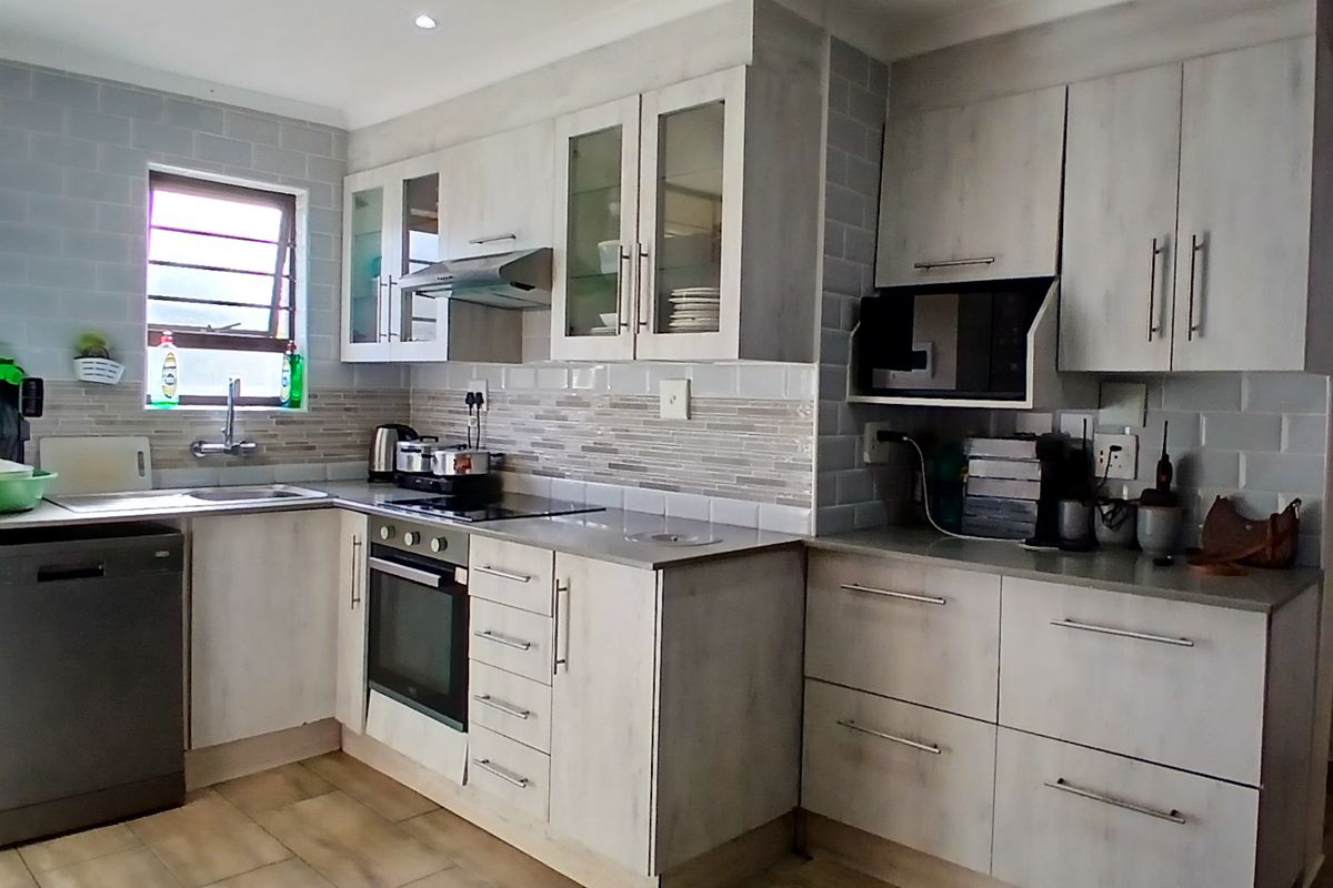 A functional kitchen featuring light-toned cabinetry, subway tile backsplash, integrated appliances including an oven and hob, and durable tiled flooring.