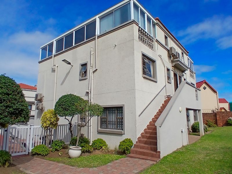 Rear view of a multi-story apartment building featuring an external staircase, enclosed upper-level balcony, and paved garden access.