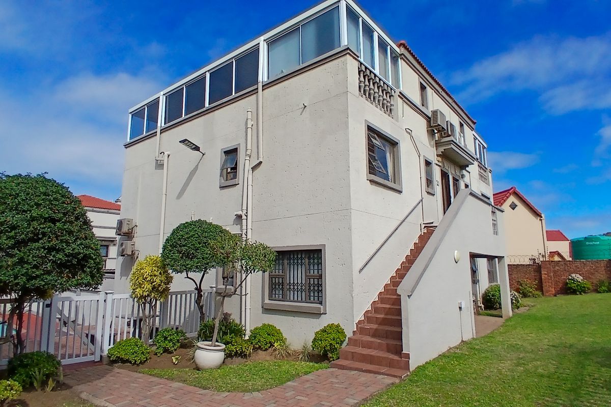 Rear view of a multi-story apartment building featuring an external staircase, enclosed upper-level balcony, and paved garden access.
