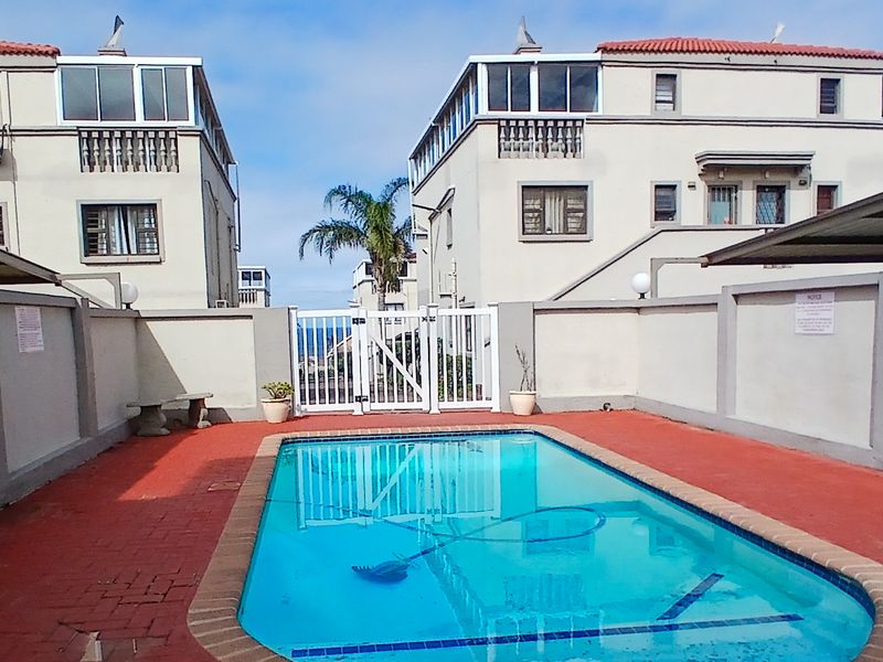 Communal swimming pool area featuring a paved deck, perimeter walling, and secure gated access within the apartment complex.