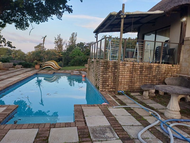 Outdoor pool area featuring a paved deck, glass balustrade, and a covered patio attached to the cottage structure.