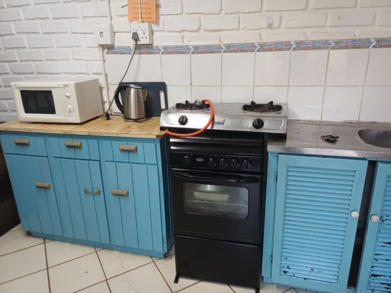 A compact kitchen featuring blue cabinetry, a gas stove with oven, tiled backsplash, and tiled flooring, showing signs of wear and dated finishes.