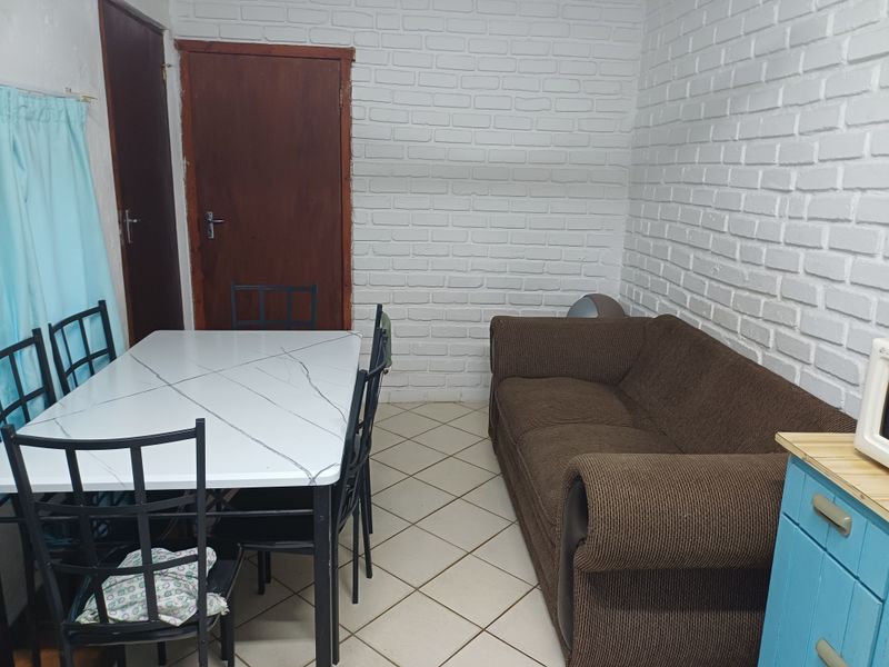 Open plan living and dining area featuring painted brick walls and ceramic floor tiles, providing a functional space for daily living.
