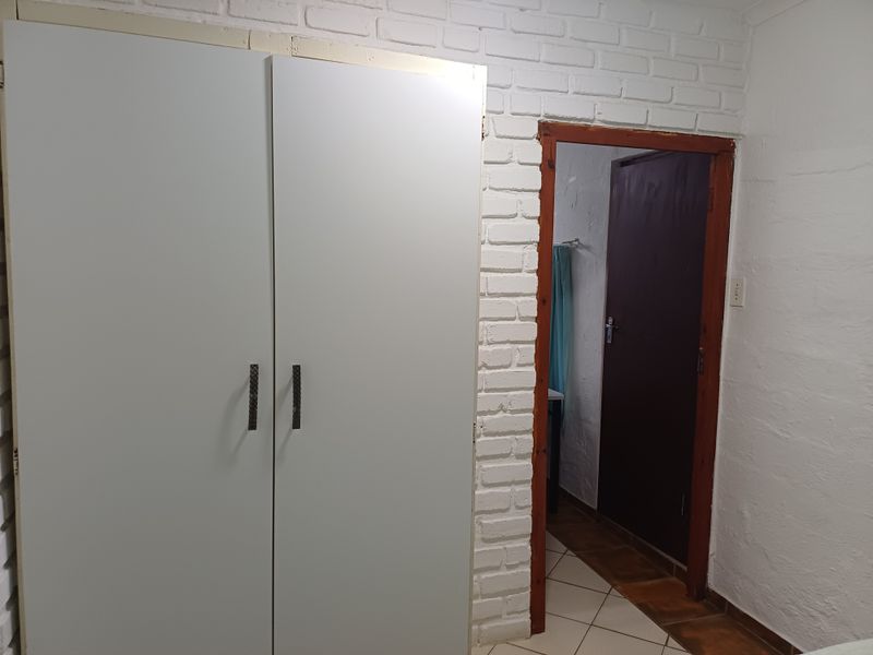 A bedroom featuring a built-in wardrobe, white painted brick walls, and tiled flooring, with an internal doorway leading to an adjacent space.