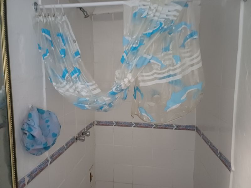 A dated shower enclosure featuring white wall tiles with a decorative border, requiring maintenance and potential modernization of fixtures and finishes.
