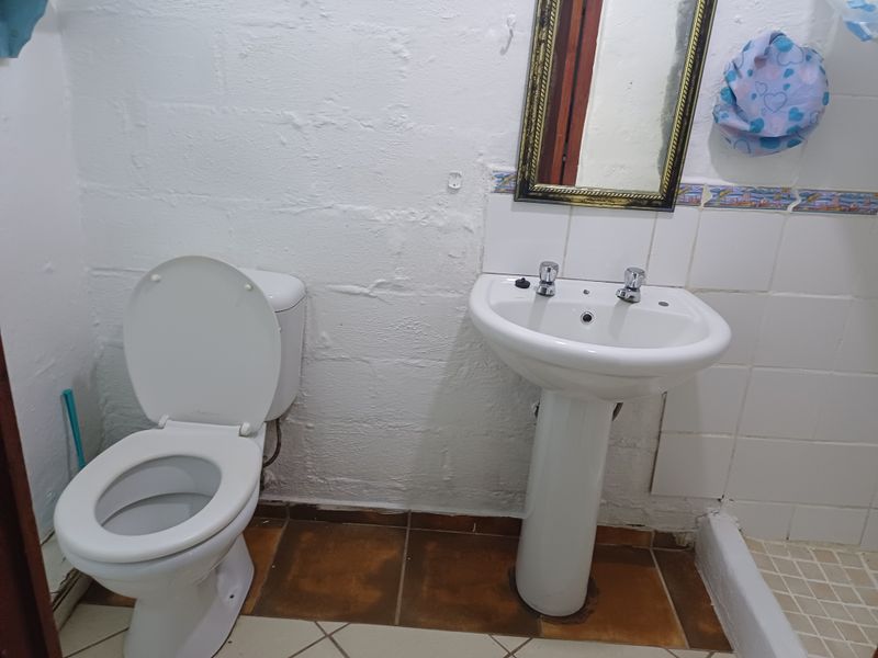 A compact bathroom featuring a pedestal basin, toilet, and shower base with dated wall and floor tiling.