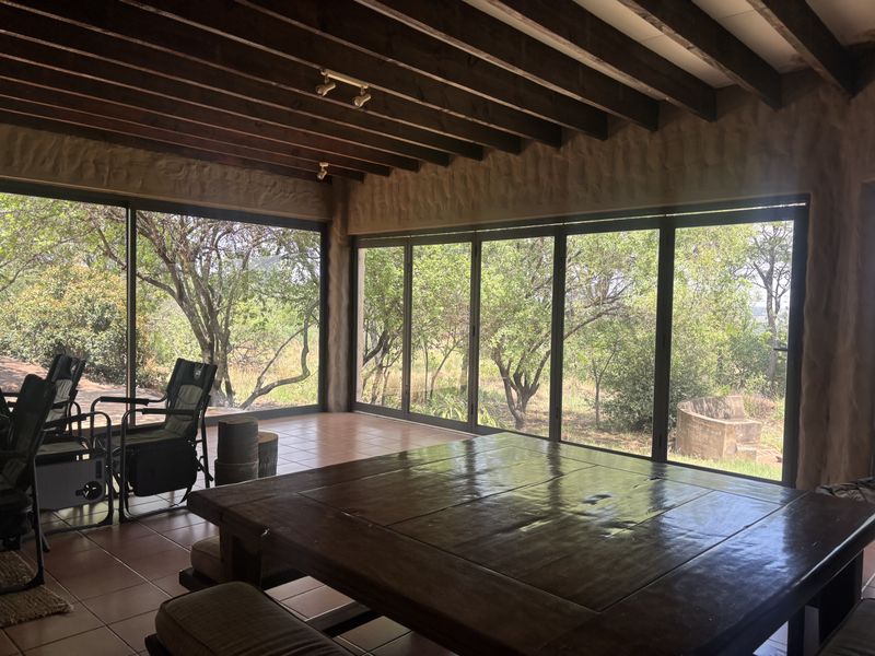 Spacious living area featuring exposed timber ceiling beams, large floor-to-ceiling glass sliding doors, and tiled flooring with views of the surrounding garden.